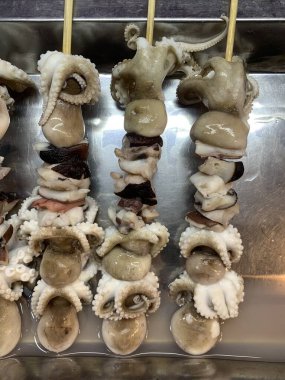 Açık hava yiyecek pazarında servis edilen bambu çubuğuyla ızgara yapılmış lezzetli kalamar ve ahtapot. egzotik Asya yemekleri. 