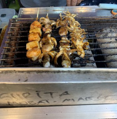 Açık hava yiyecek pazarında servis edilen bambu çubuğuyla ızgara yapılmış lezzetli kalamar ve ahtapot. egzotik Asya yemekleri. 