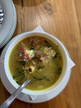 Kırmızı Snapper balığı baharatlı çorba sarımsak, domates, sebze ve acı biber sosu ve ahşap masadaki çeşitli baharatlarla dolu beyaz bir kasede ekşi köri. Lezzetli yemek.