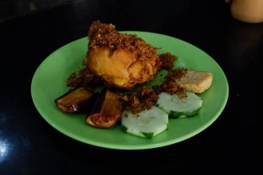 Ayam bakar Penyet, taze sebze, salatalık ve fesleğen yapraklı sıcak biberli kızarmış tavuktur.