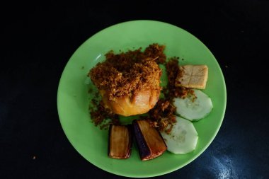 Ayam bakar Penyet is a fried chicken served with hot chili in a plate with fresh vegetables, slices of cucumber and basil leaves clipart