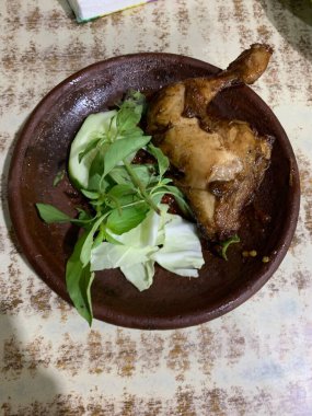Ayam bakar Penyet, taze sebze, salatalık ve fesleğen yapraklı sıcak biberli kızarmış tavuktur.