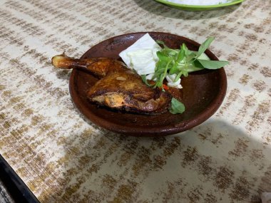 Ayam bakar Penyet is a fried chicken served with hot chili in a plate with fresh vegetables, slices of cucumber and basil leaves clipart