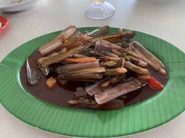 Bahar soğanı ve yeşil tabakta kızarmış sarımsakla süslenmiş tatlı ve ekşi soslu Çin usulü bambu midyesi.