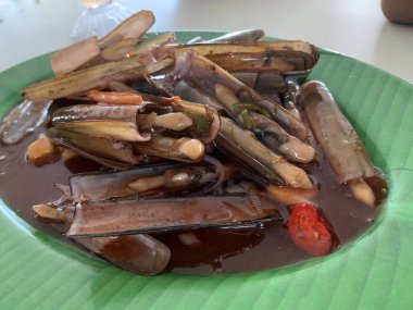 Bahar soğanı ve yeşil tabakta kızarmış sarımsakla süslenmiş tatlı ve ekşi soslu Çin usulü bambu midyesi.