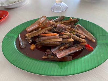 Bahar soğanı ve yeşil tabakta kızarmış sarımsakla süslenmiş tatlı ve ekşi soslu Çin usulü bambu midyesi.