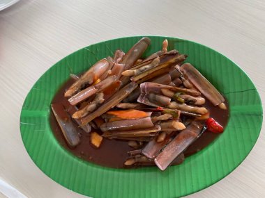 Bahar soğanı ve yeşil tabakta kızarmış sarımsakla süslenmiş tatlı ve ekşi soslu Çin usulü bambu midyesi.