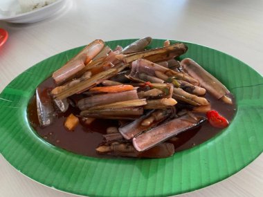 Bahar soğanı ve yeşil tabakta kızarmış sarımsakla süslenmiş tatlı ve ekşi soslu Çin usulü bambu midyesi.