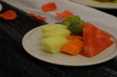 Kahvaltıda beyaz tabakta tropikal konseptle karışık taze meyve yakın çekim. Bir sürü karpuz, kavun, üzüm, ananas. ve papaya. seçici odak.