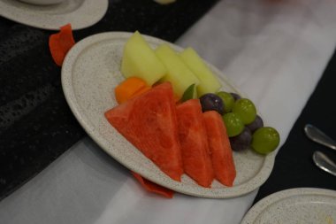 Kahvaltıda beyaz tabakta tropikal konseptle karışık taze meyve yakın çekim. Bir sürü karpuz, kavun, üzüm, ananas. ve papaya. seçici odak.