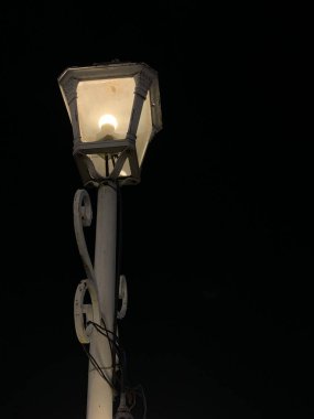 Eski demir antika dekoratif duvar lambası gecenin bir yarısı küçük bir kasabada bir bina duvarında yanıyor. Eski konsept.