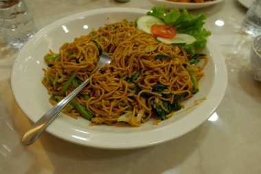 Pişmiş erişteyle kızartılmış beyaz tabak yeşil sebzeler taze marul, salatalık, brokoli ve domates dilimi ile karıştırılmış tavuk, yumurta veya tofu ile süslenmiş. Çatal eriştenin üstüne konur..