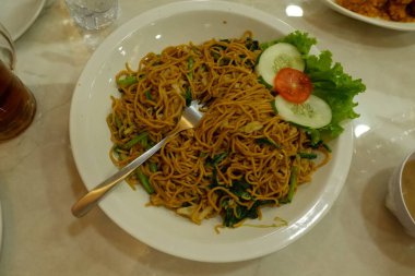 Pişmiş erişteyle kızartılmış beyaz tabak yeşil sebzeler taze marul, salatalık, brokoli ve domates dilimi ile karıştırılmış tavuk, yumurta veya tofu ile süslenmiş. Çatal eriştenin üstüne konur..