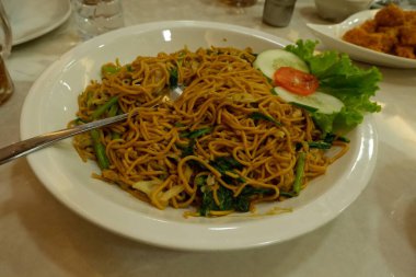 Pişmiş erişteyle kızartılmış beyaz tabak yeşil sebzeler taze marul, salatalık, brokoli ve domates dilimi ile karıştırılmış tavuk, yumurta veya tofu ile süslenmiş. Çatal eriştenin üstüne konur..