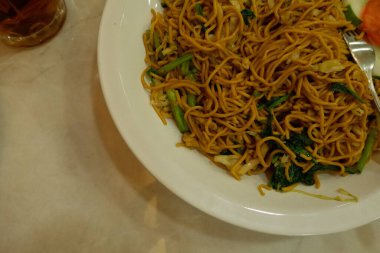 Pişmiş erişteyle kızartılmış beyaz tabak yeşil sebzeler taze marul, salatalık, brokoli ve domates dilimi ile karıştırılmış tavuk, yumurta veya tofu ile süslenmiş. Çatal eriştenin üstüne konur..