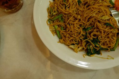 Pişmiş erişteyle kızartılmış beyaz tabak yeşil sebzeler taze marul, salatalık, brokoli ve domates dilimi ile karıştırılmış tavuk, yumurta veya tofu ile süslenmiş. Çatal eriştenin üstüne konur..