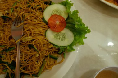 Pişmiş erişteyle kızartılmış beyaz tabak yeşil sebzeler taze marul, salatalık, brokoli ve domates dilimi ile karıştırılmış tavuk, yumurta veya tofu ile süslenmiş. Çatal eriştenin üstüne konur..