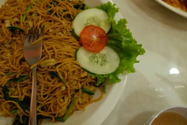 Pişmiş erişteyle kızartılmış beyaz tabak yeşil sebzeler taze marul, salatalık, brokoli ve domates dilimi ile karıştırılmış tavuk, yumurta veya tofu ile süslenmiş. Çatal eriştenin üstüne konur..