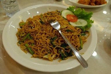 Pişmiş erişteyle kızartılmış beyaz tabak yeşil sebzeler taze marul, salatalık, brokoli ve domates dilimi ile karıştırılmış tavuk, yumurta veya tofu ile süslenmiş. Çatal eriştenin üstüne konur..