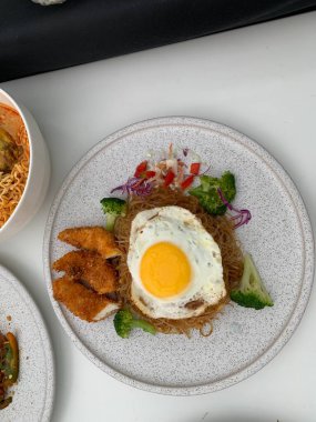 Pişmiş erişteyle kızartılmış beyaz tabak yeşil sebzeler taze marul, salatalık, brokoli ve domates dilimi ile karıştırılmış tavuk, yumurta veya tofu ile süslenmiş. Çatal eriştenin üstüne konur..