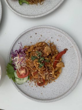 Pişmiş erişteyle kızartılmış beyaz tabak yeşil sebzeler taze marul, salatalık, brokoli ve domates dilimi ile karıştırılmış tavuk, yumurta veya tofu ile süslenmiş. Çatal eriştenin üstüne konur..