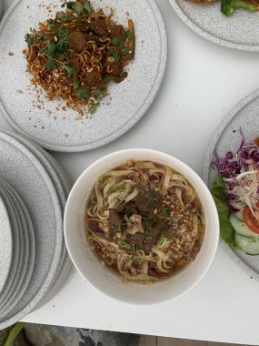 Pişmiş erişteyle kızartılmış beyaz tabak yeşil sebzeler taze marul, salatalık, brokoli ve domates dilimi ile karıştırılmış tavuk, yumurta veya tofu ile süslenmiş. Çatal eriştenin üstüne konur..