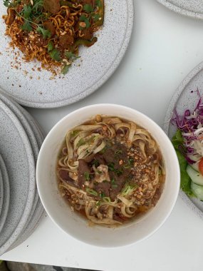 Pişmiş erişteyle kızartılmış beyaz tabak yeşil sebzeler taze marul, salatalık, brokoli ve domates dilimi ile karıştırılmış tavuk, yumurta veya tofu ile süslenmiş. Çatal eriştenin üstüne konur..