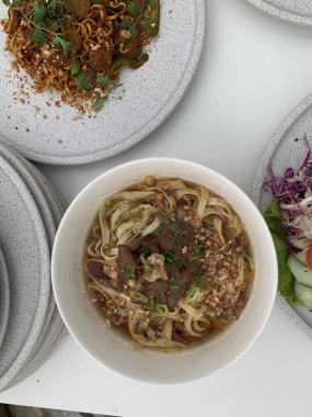 Pişmiş erişteyle kızartılmış beyaz tabak yeşil sebzeler taze marul, salatalık, brokoli ve domates dilimi ile karıştırılmış tavuk, yumurta veya tofu ile süslenmiş. Çatal eriştenin üstüne konur..