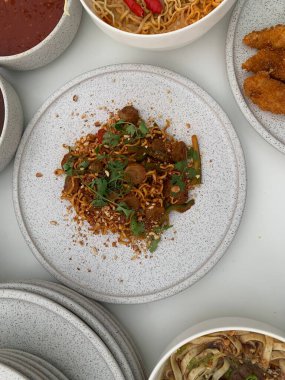 Pişmiş erişteyle kızartılmış beyaz tabak yeşil sebzeler taze marul, salatalık, brokoli ve domates dilimi ile karıştırılmış tavuk, yumurta veya tofu ile süslenmiş. Çatal eriştenin üstüne konur..