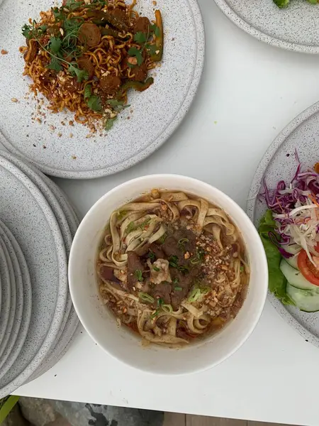 Pişmiş erişteyle kızartılmış beyaz tabak yeşil sebzeler taze marul, salatalık, brokoli ve domates dilimi ile karıştırılmış tavuk, yumurta veya tofu ile süslenmiş. Çatal eriştenin üstüne konur..