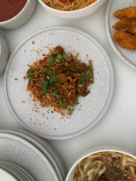 Pişmiş erişteyle kızartılmış beyaz tabak yeşil sebzeler taze marul, salatalık, brokoli ve domates dilimi ile karıştırılmış tavuk, yumurta veya tofu ile süslenmiş. Çatal eriştenin üstüne konur..