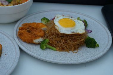 Pişmiş erişteyle kızartılmış beyaz tabak yeşil sebzeler taze marul, salatalık, brokoli ve domates dilimi ile karıştırılmış tavuk, yumurta veya tofu ile süslenmiş. Çatal eriştenin üstüne konur..