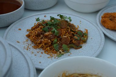 Pişmiş erişteyle kızartılmış beyaz tabak yeşil sebzeler taze marul, salatalık, brokoli ve domates dilimi ile karıştırılmış tavuk, yumurta veya tofu ile süslenmiş. Çatal eriştenin üstüne konur..