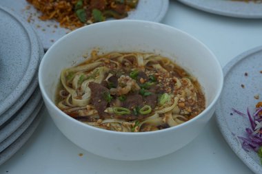 Pişmiş erişteyle kızartılmış beyaz tabak yeşil sebzeler taze marul, salatalık, brokoli ve domates dilimi ile karıştırılmış tavuk, yumurta veya tofu ile süslenmiş. Çatal eriştenin üstüne konur..