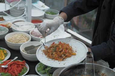 Pişmiş erişteyle kızartılmış beyaz tabak yeşil sebzeler taze marul, salatalık, brokoli ve domates dilimi ile karıştırılmış tavuk, yumurta veya tofu ile süslenmiş. Çatal eriştenin üstüne konur..
