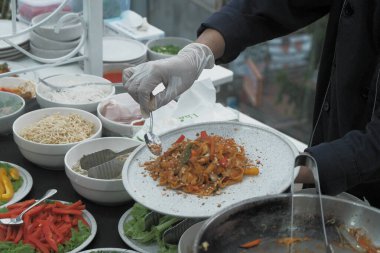 Pişmiş erişteyle kızartılmış beyaz tabak yeşil sebzeler taze marul, salatalık, brokoli ve domates dilimi ile karıştırılmış tavuk, yumurta veya tofu ile süslenmiş. Çatal eriştenin üstüne konur..