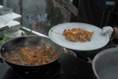Pişmiş erişteyle kızartılmış beyaz tabak yeşil sebzeler taze marul, salatalık, brokoli ve domates dilimi ile karıştırılmış tavuk, yumurta veya tofu ile süslenmiş. Çatal eriştenin üstüne konur..
