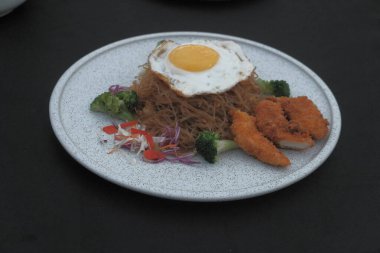 Pişmiş erişteyle kızartılmış beyaz tabak yeşil sebzeler taze marul, salatalık, brokoli ve domates dilimi ile karıştırılmış tavuk, yumurta veya tofu ile süslenmiş. Çatal eriştenin üstüne konur..