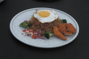 Pişmiş erişteyle kızartılmış beyaz tabak yeşil sebzeler taze marul, salatalık, brokoli ve domates dilimi ile karıştırılmış tavuk, yumurta veya tofu ile süslenmiş. Çatal eriştenin üstüne konur..