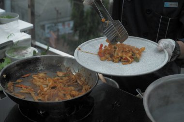 Pişmiş erişteyle kızartılmış beyaz tabak yeşil sebzeler taze marul, salatalık, brokoli ve domates dilimi ile karıştırılmış tavuk, yumurta veya tofu ile süslenmiş. Çatal eriştenin üstüne konur..