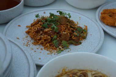 Pişmiş erişteyle kızartılmış beyaz tabak yeşil sebzeler taze marul, salatalık, brokoli ve domates dilimi ile karıştırılmış tavuk, yumurta veya tofu ile süslenmiş. Çatal eriştenin üstüne konur..