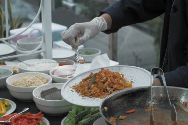Pişmiş erişteyle kızartılmış beyaz tabak yeşil sebzeler taze marul, salatalık, brokoli ve domates dilimi ile karıştırılmış tavuk, yumurta veya tofu ile süslenmiş. Çatal eriştenin üstüne konur..