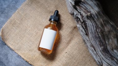 Siyah damperli kapaklı küçük bir cam şişe aşınmış ahşap parçasına dayanır, kehribar renkli bir sıvı içerir ve boş beyaz etiket içerir..