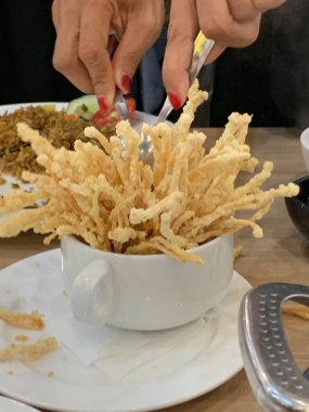 Çıtır çıtır kızarmış enoki mantarları, yanında taze marul dilimlenmiş yeşil soğan ve doğranmış kırmızı biber ile birlikte beyaz tabakta düzenlenir.. 