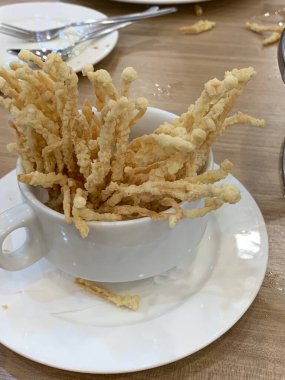 Çıtır çıtır kızarmış enoki mantarları, yanında taze marul dilimlenmiş yeşil soğan ve doğranmış kırmızı biber ile birlikte beyaz tabakta düzenlenir.. 