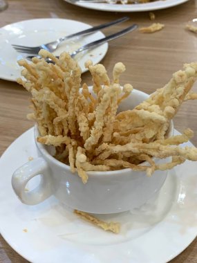 Çıtır çıtır kızarmış enoki mantarları, yanında taze marul dilimlenmiş yeşil soğan ve doğranmış kırmızı biber ile birlikte beyaz tabakta düzenlenir.. 