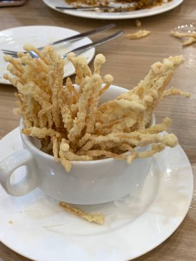 Çıtır çıtır kızarmış enoki mantarları, yanında taze marul dilimlenmiş yeşil soğan ve doğranmış kırmızı biber ile birlikte beyaz tabakta düzenlenir.. 