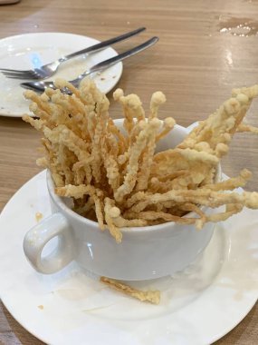 Çıtır çıtır kızarmış enoki mantarları, yanında taze marul dilimlenmiş yeşil soğan ve doğranmış kırmızı biber ile birlikte beyaz tabakta düzenlenir.. 