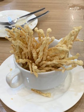 Çıtır çıtır kızarmış enoki mantarları, yanında taze marul dilimlenmiş yeşil soğan ve doğranmış kırmızı biber ile birlikte beyaz tabakta düzenlenir.. 