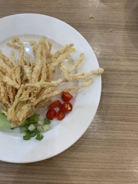 Çıtır çıtır kızarmış enoki mantarları, yanında taze marul dilimlenmiş yeşil soğan ve doğranmış kırmızı biber ile birlikte beyaz tabakta düzenlenir.. 